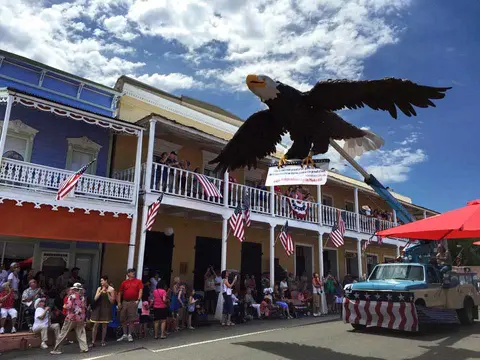 A large eagle float is driven down a street during a parade with a crowd watching.