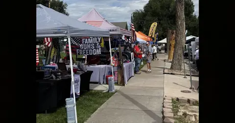 People walking along booths set up outdoors under tents.
