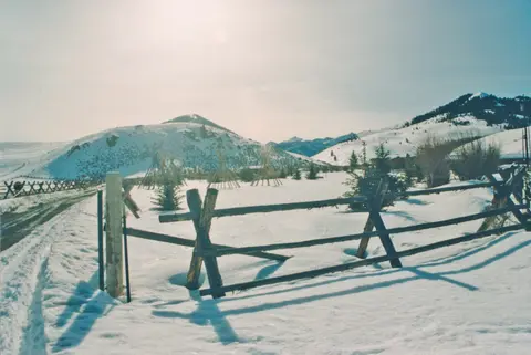A snowy landscape with mountains and a wooden fence.