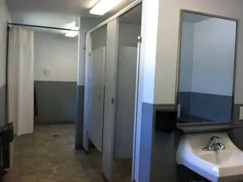 An interior view of a public restroom with stalls, sinks, and a shower area.