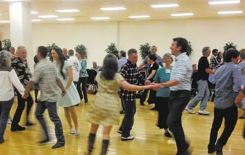 A group of people dancing in a hall with a wooden floor.