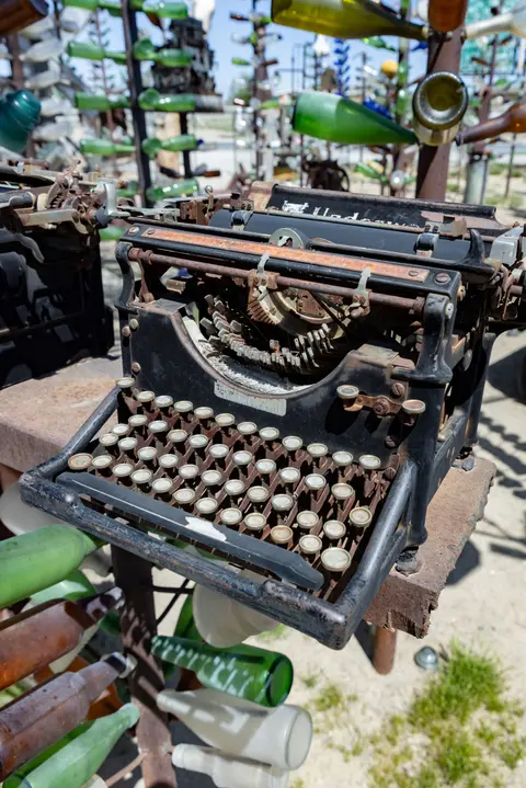 An old rusty typewriter is displayed outdoors with glass bottles in the background.
