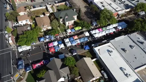 An aerial view shows an outdoor market with many tents set up along a street.
