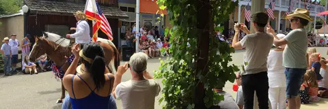 People watch a parade featuring horses and flags on a street.