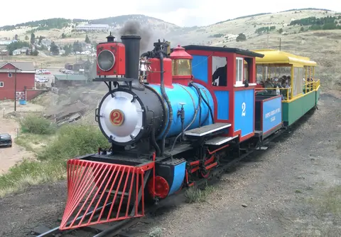 A colorful steam locomotive with passenger cars on tracks in a hilly landscape.