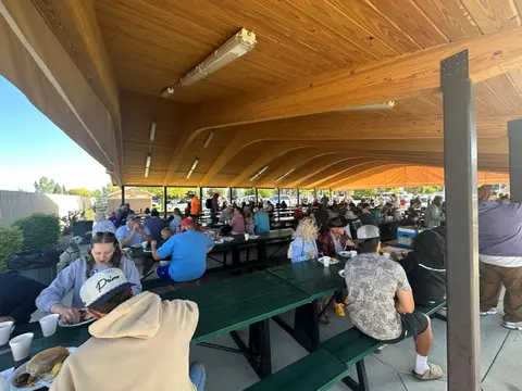 A large group of people gather under a covered pavilion for a meal.