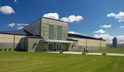 A modern concrete building with a large green lawn under a blue sky.