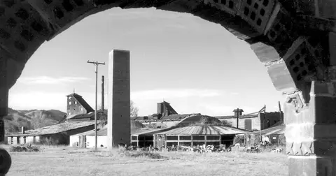 Black and white photo of industrial buildings viewed through an arched opening.