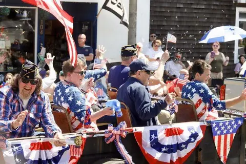 People ride in a parade float decorated with American flags and bunting.