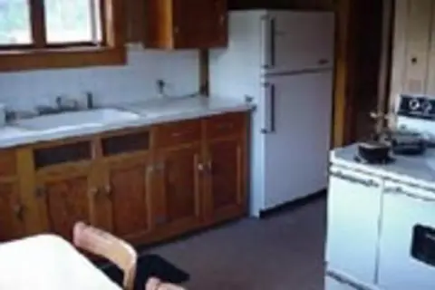An interior view of a rustic kitchen with wooden cabinets and white appliances.