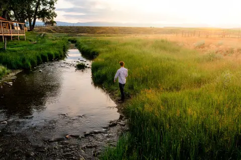 A person fishes in a narrow stream at sunset.