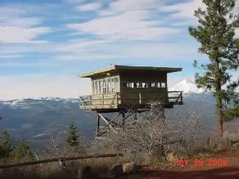 A lookout tower stands on a mountainside overlooking a distant valley.