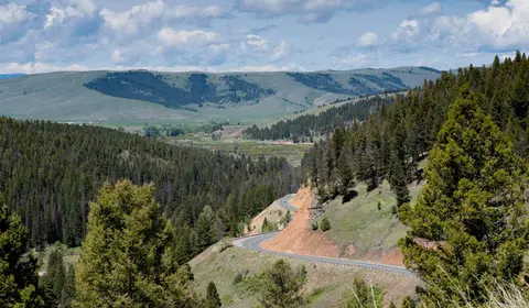 A winding road descends through a forested mountain valley under a cloudy sky.