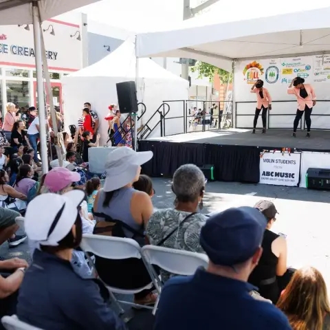 An audience watches two performers on a stage under a tent.