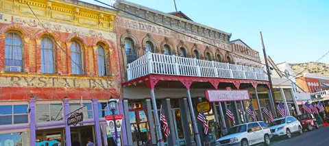 An exterior view of historic brick buildings with American flags and parked cars on a sunny day.