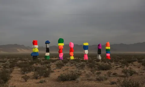 A row of brightly painted stacked boulders stands in a desert landscape.