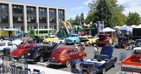 An outdoor car show featuring classic cars, food trucks, and bounce houses.