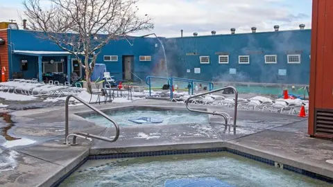 An outdoor hot tub and pool area with steam rising, surrounded by snow.