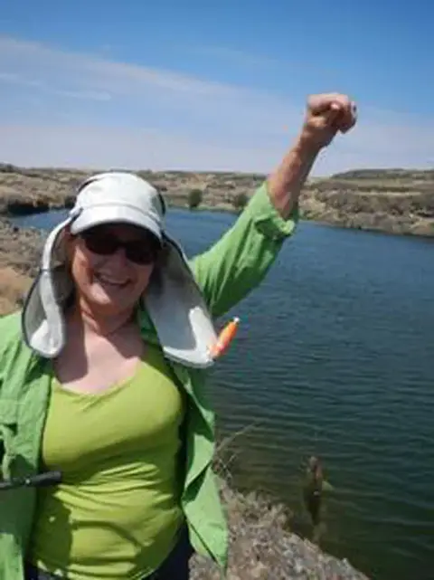 A woman smiles while fishing by a river.
