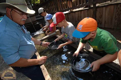A man helps children pan for gold in a water trough.