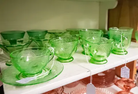 A shelf display of green glassware and teacups with price tags.