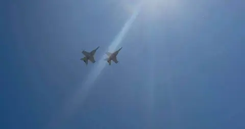Two fighter jets fly in formation against a bright blue sky.
