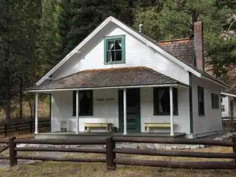 A white house with a front porch and a wooden fence stands among trees.
