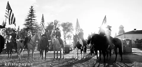Black and white photo of people on horseback holding American flags.
