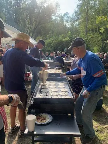 People cooking pancakes on a large outdoor griddle at an event.