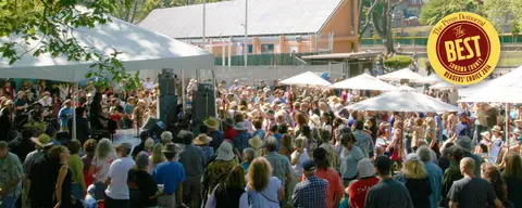 A large crowd gathers to watch a band perform under a tent outdoors.