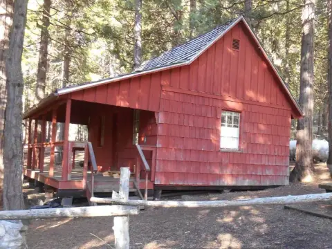 A red wooden cabin sits among tall trees in a forest.