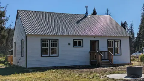 A white cabin with a metal roof and a small wooden porch stands outdoors.