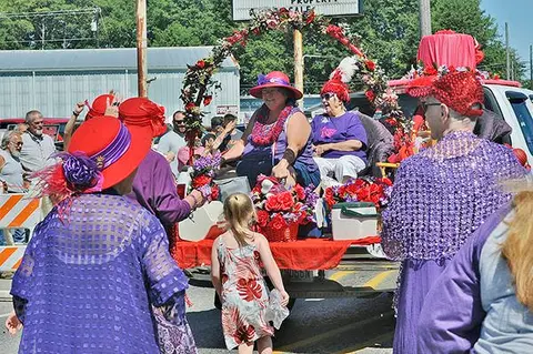People dressed in colorful outfits and hats participate in an outdoor parade.