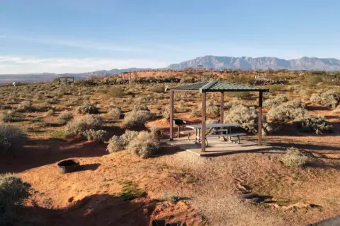 A covered picnic table sits in a desert landscape with mountains in the background.