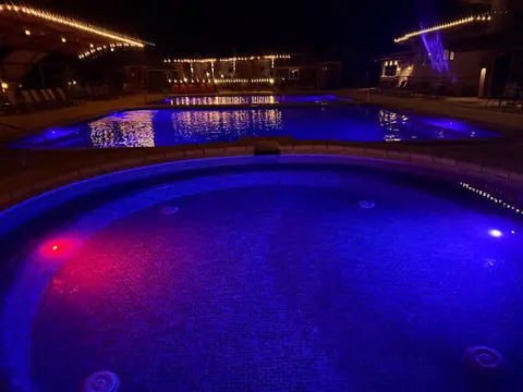 A nighttime view of illuminated outdoor swimming pools and a hot tub.