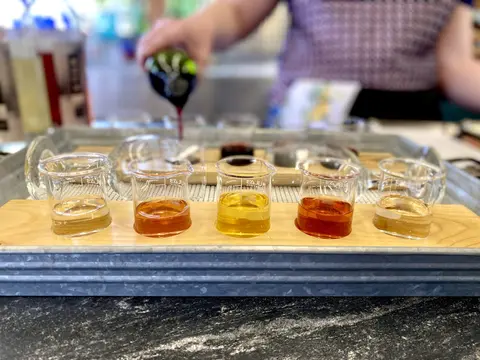 A flight of drinks served in small beakers on a wooden board.