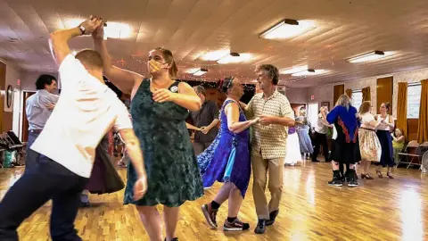 People dancing inside a hall with wooden floors.