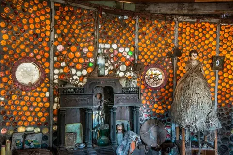 Interior view of a building with walls made of amber glass bottles and various decorative objects.