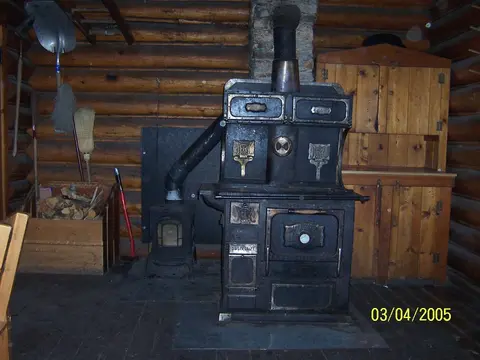 A vintage wood-burning stove stands inside a log cabin.