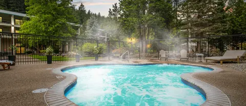 A hot spring pool with steam rising, surrounded by trees and a fence.
