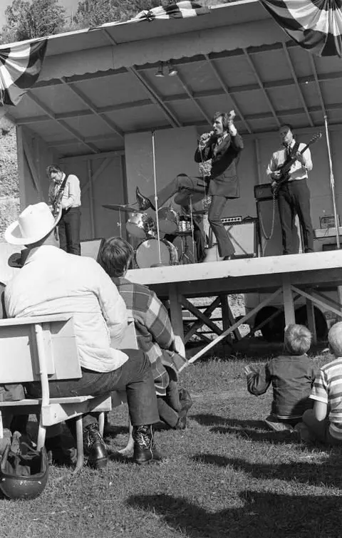 A band performs on an outdoor stage while an audience watches.