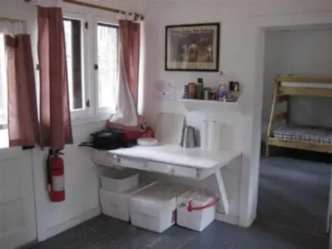 An interior view of a room with a small counter, storage bins, and a doorway leading to a bedroom with bunk beds.