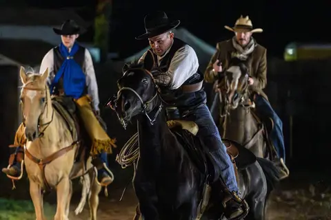 Three cowboys ride horses outdoors at night.