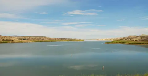 A scenic view of a calm lake under a cloudy blue sky.