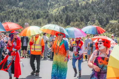 People walking in an outdoor parade holding colorful umbrellas.