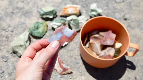 A hand holds up a piece of agate with an orange cup filled with more rocks nearby.