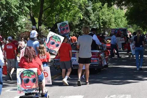People walking alongside a convertible car in a parade.