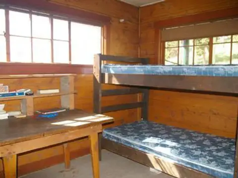 An interior view of a rustic wooden room with a bunk bed and a desk.