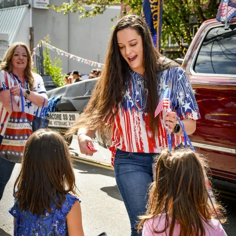 A woman distributes small flags to children during an outdoor event.