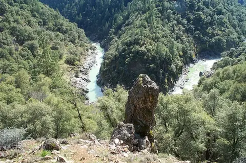 A high-angle view of a river winding through a forested canyon with a prominent rock formation in the foreground.